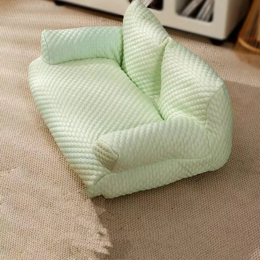 Canapé pour chat en tissu matelassé vert clair sur tapis beige. Lit pour animaux de compagnie, design moderne, confort et style pour chats.